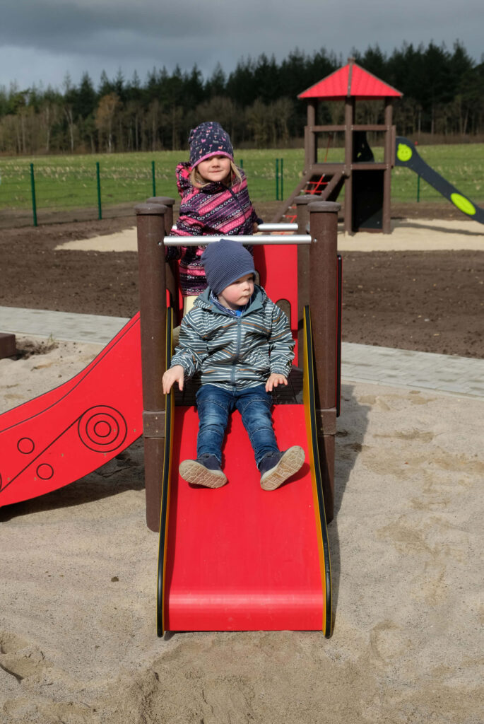 Zwei Kinder spielen auf einem Spielplatz auf einem niedrigem Turm mit Rutsche