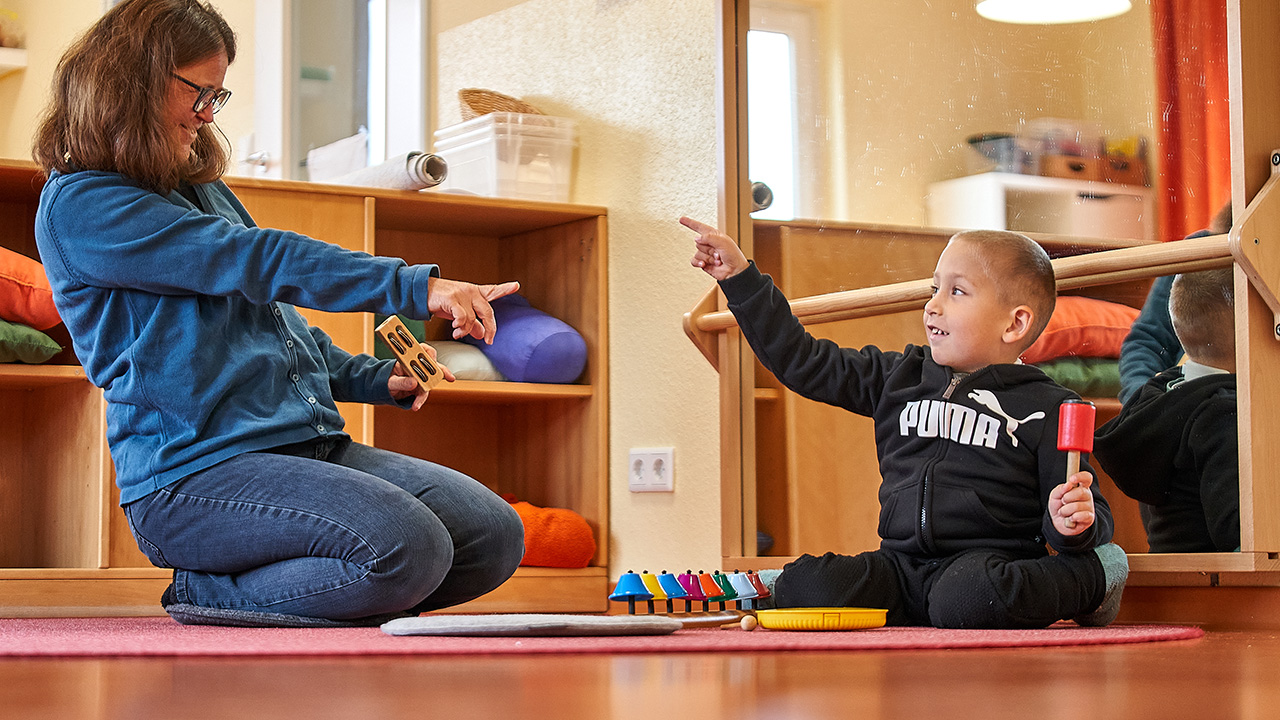 Eine Frau und ein Kind sitzen gemeinsam auf einem Teppisch und zeigen gegenseitig aufeinander