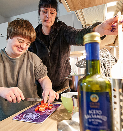 Ein Bewohner schneidet Tomaten neben dem Herd. Eine Frau, die neben ihm steht schaut zu