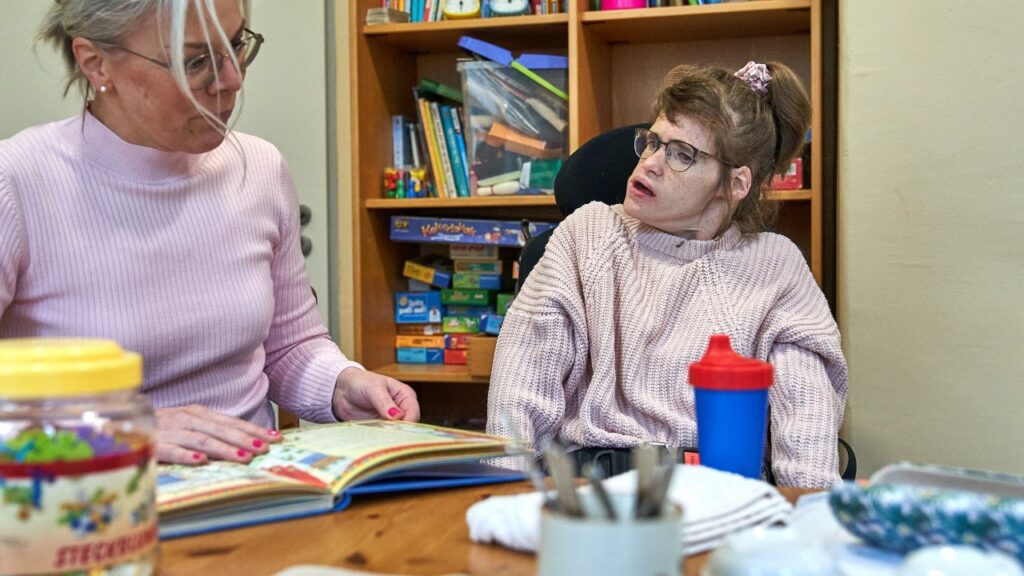 Zwei Frauen sitzen an einem Tisch und lesen ein Buch zusammen