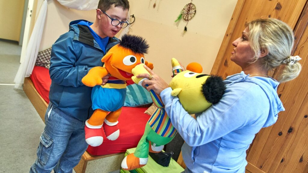 Ein Teenager und eine Frau stehen sich mit Ernie und Bert Puppen in den Händen gegenüber