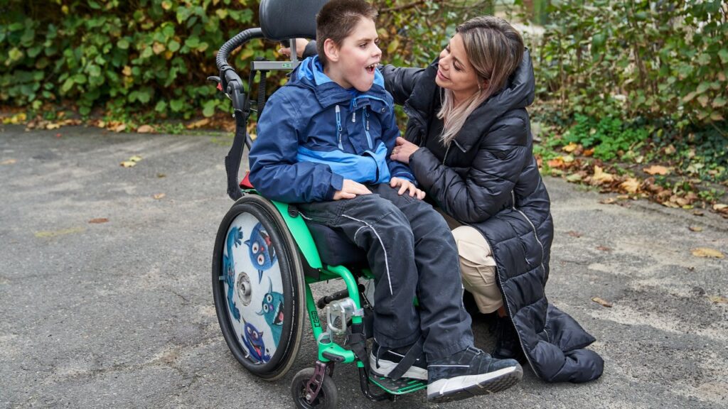 Eine Frau hockt neben einem Bewohner, der im Rollstuhl sitzt und schaut ihn dabei an