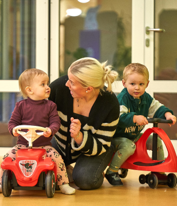 Eine Frau sitzt zwischen zwei Kindern, die auf Laufrädern sitzen